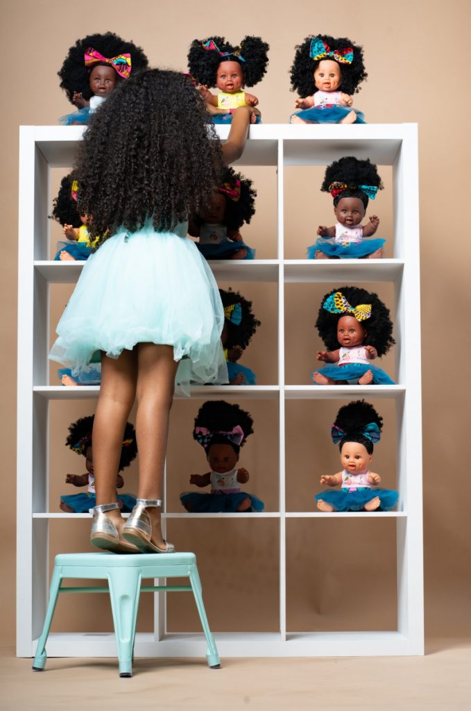Black girl selects a doll from a shelf full of Black dolls with curly hair